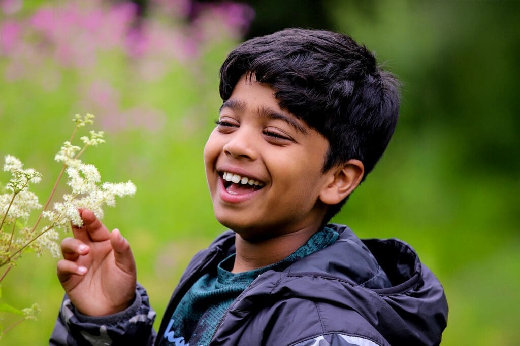 Aneeshwar_2 Aneeshwar laughs alongside white flowers on a green background