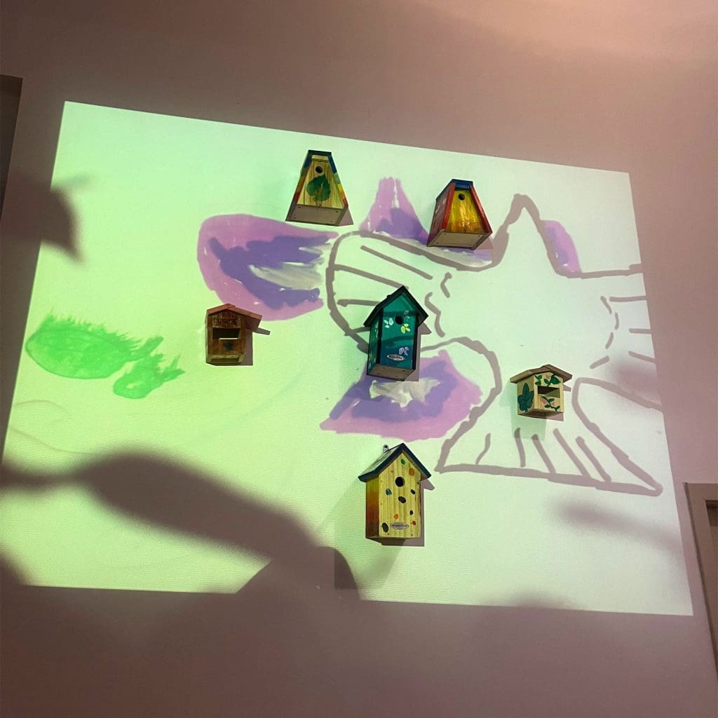 Bird-boxes A piece of bird-inspired art: six bird boxes attached to a wall, arranged in a pentagon, with a painting of a bird projected over them